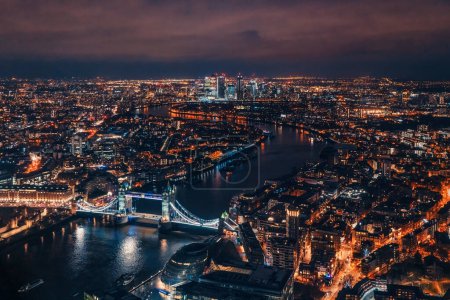Téléchargez les photos : Vue aérienne de nuit du Tower Bridge au-dessus de la Tamise, bâtiments éclairés luisant dans l'obscurité - en image libre de droit