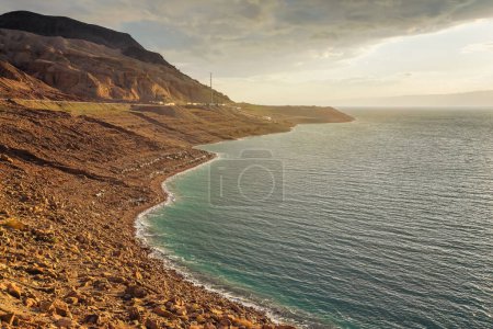 Téléchargez les photos : Côte de la mer Morte côté Jordanie, sable sec et rochers plage escarpée, soleil de l'après-midi brille sur la surface de l'eau calme - en image libre de droit