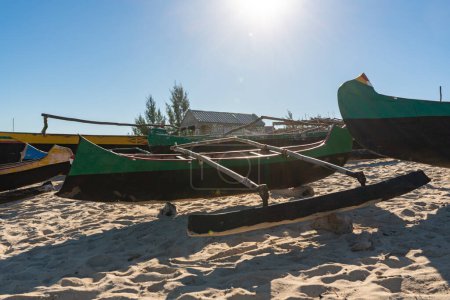 Des bateaux de pêche simples sur une plage de sable près d'un petit village de Madagascar, le soleil brille en arrière-plan