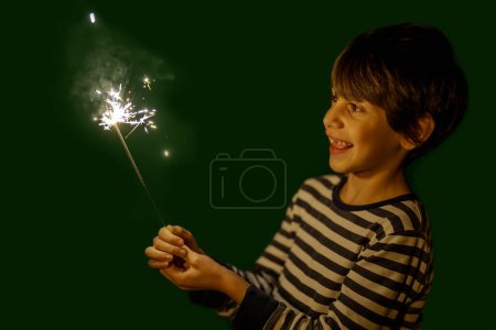 Foto de Lindo chico sosteniendo fuegos artificiales, mirando emocionado, fondo verde - Imagen libre de derechos