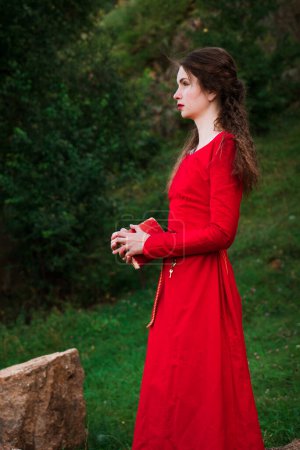 Téléchargez les photos : Vintage portrait of a beautiful noble lady in a red dress with a book in the garden. Historical reconstruction of the Victorian era. - en image libre de droit