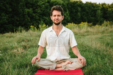 Foto de Un joven haciendo yoga en la naturaleza con una sonrisa, sentado en la posición de loto - Imagen libre de derechos
