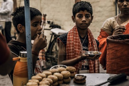 Foto de Rishikesh, 2017, niño indio con su madre y su hermano comen comida callejera en la feria, mercado del pueblo - Imagen libre de derechos