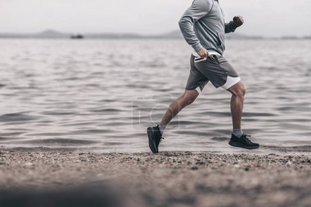 Foto de Estilo de vida saludable joven fitness hombre corriendo en la playa junto al mar. Entrenamiento al aire libre, Concepto de estilo de vida saludable. - Imagen libre de derechos