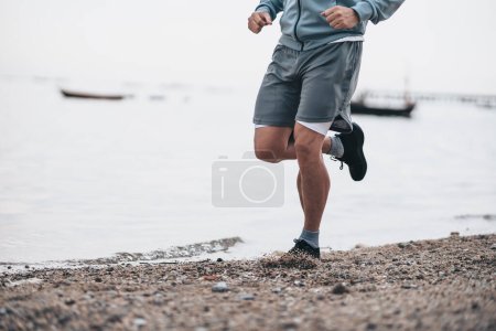 Foto de Estilo de vida saludable joven fitness hombre corriendo en la playa junto al mar. Entrenamiento al aire libre, Concepto de estilo de vida saludable. - Imagen libre de derechos
