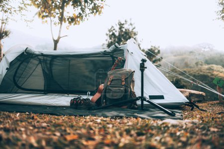 Téléchargez les photos : Matériel de camping, sacs, chaussures, ukulélé, trépied à côté de la tente le matin. Camp d'objets, concept de voyage et de vocation. - en image libre de droit