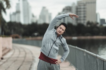 Ein Mann dehnt seine Muskeln im Stadtpark, bevor er Cardio-Workout macht und läuft. Gesundheit und Lifestyle in der Großstadt.