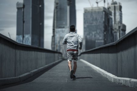 Ein Mann läuft auf einer Fußgängerbrücke im Stadtpark zum Ausdauertraining. Gesundheit und Lifestyle in der Großstadt.