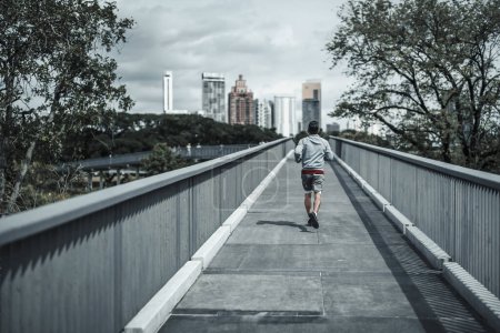 Foto de Un hombre corriendo por la pasarela en el parque del centro de la ciudad para hacer ejercicio cardiovascular. Salud y estilo de vida en la gran ciudad concepto de vida. - Imagen libre de derechos