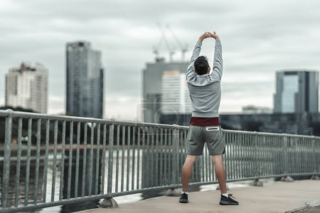 Foto de Un hombre estirando su músculo en el parque del centro de la ciudad antes del entrenamiento cardiovascular, corriendo. Salud y estilo de vida en la gran ciudad concepto de vida. - Imagen libre de derechos