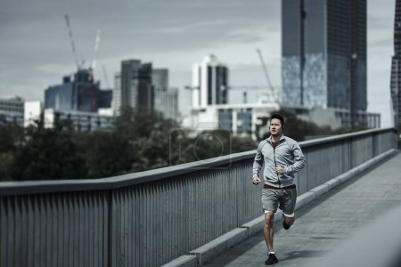 Ein Mann läuft auf einer Fußgängerbrücke im Stadtpark zum Ausdauertraining. Gesundheit und Lifestyle in der Großstadt.