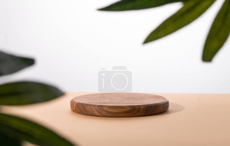 Empty podium with a palm leaf. A round wooden stage on a beige table. Minimal abstract background for product presentation. Copy space.