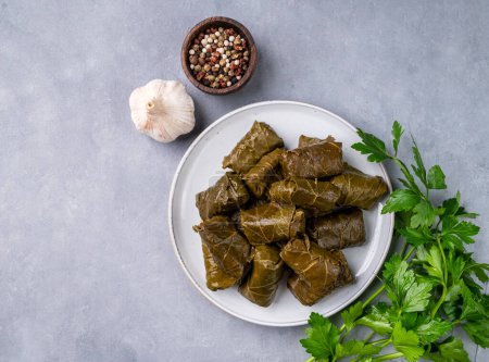 Dolma. Stuffed grape leaves (traditional Caucasian, Turkish, Greek cuisine) on a blue plate with fresh herbs on a light background with garlic and pepper. Top view and copy space.