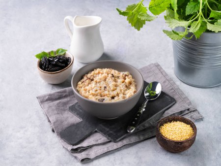 Téléchargez les photos : Porridge de millet aux pruneaux dans un bol sur fond bleu avec du lait. Le concept d'un délicieux, nutritif et sain petit déjeuner. Aliments diététiques et énergétiques. - en image libre de droit