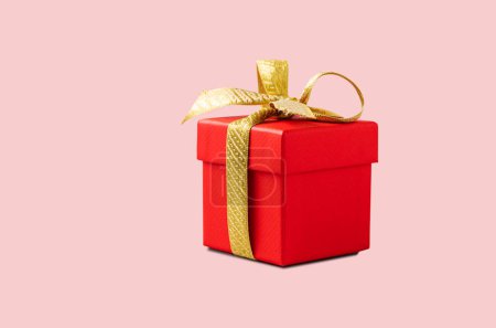 Foto de Una caja de regalo roja con una cinta de oro sobre un fondo rosa sin sombra. El concepto de fotografía navideña. Sorpresa para San Valentín, cumpleaños, boda. Copiar espacio y vista frontal. - Imagen libre de derechos