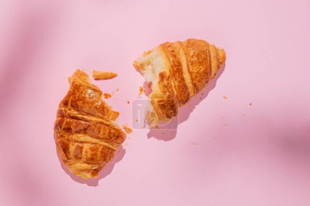Couché plat de croissant frais cassé sur fond rose avec ombre. Aménagement créatif et concept d'alimentation saine et petit déjeuner français. Vue du dessus et espace de copie.