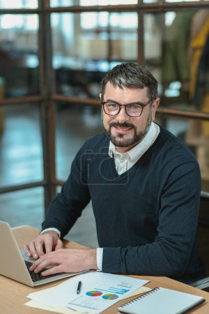 Téléchargez les photos : Portrait of adult businessman sitting in small modern office and looking at camera - en image libre de droit