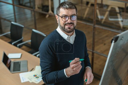 Téléchargez les photos : Happy adult businessman writing on a whiteboard using a marker pen in the office - en image libre de droit
