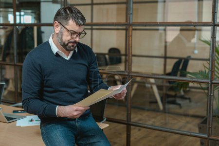 Téléchargez les photos : Businessman in glasses analyzes documents in his hands while working in the office - en image libre de droit