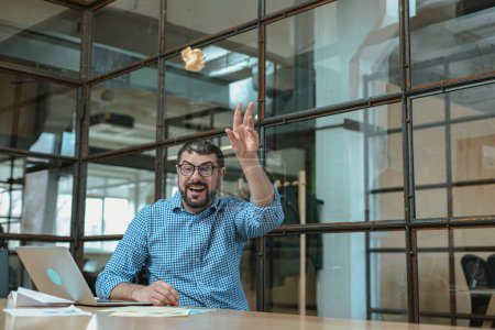 Foto de Sonriente hombre de negocios lanzando papeles en la oficina mientras trabaja con el ordenador portátil - Imagen libre de derechos