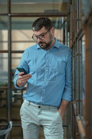 Téléchargez les photos : Businessman holding and using cell phone mobile apps while standing in office - en image libre de droit
