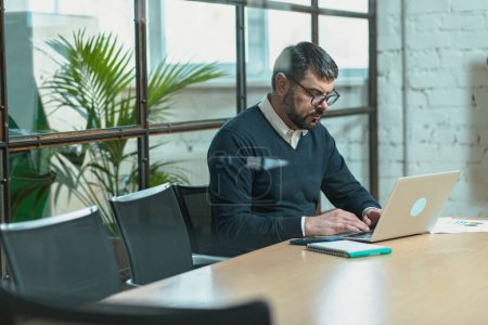 Téléchargez les photos : Gestionnaire masculin regardant l'écran et tapant sur ordinateur portable tout en travaillant sur son lieu de travail - en image libre de droit