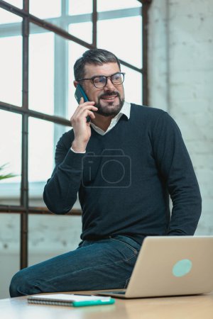 Foto de Hombre de negocios sonriente en la oficina hablando por teléfono mientras está sentado en el escritorio - Imagen libre de derechos