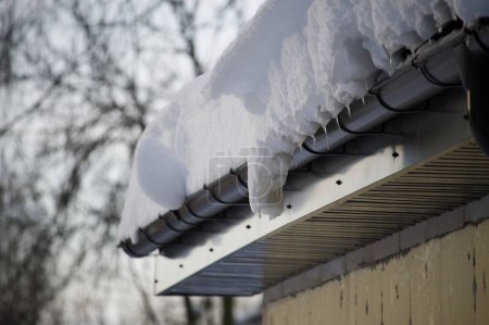 Téléchargez les photos : Gouttière couverte de neige remplie dans une large mesure de neige, même près du bord du toit - en image libre de droit