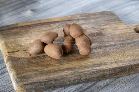 Foto de Escena rústica de un grupo de frutas de tamarindo dulce marrón esparcidas por una superficie de madera con diferentes tonos de gris - Imagen libre de derechos