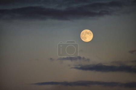 Téléchargez les photos : La pleine lune émet une douce lueur jaunâtre dans un ciel crépusculaire avec un assortiment de nuages autour d'elle - en image libre de droit