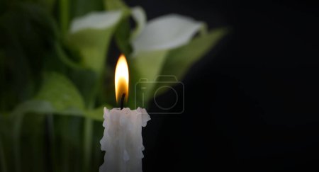 Téléchargez les photos : Bougie blanche avec une flamme jaune devant des lys calla blancs contrastant avec le fond sombre - en image libre de droit