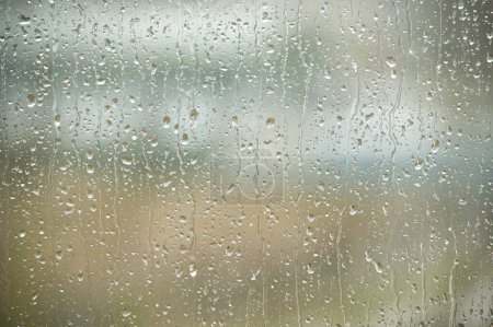 Téléchargez les photos : Des gouttelettes se précipitent d'une bruine à l'extérieur dispersée à travers une fenêtre. Tranquillité et solitude souvent associées aux jours de pluie - en image libre de droit