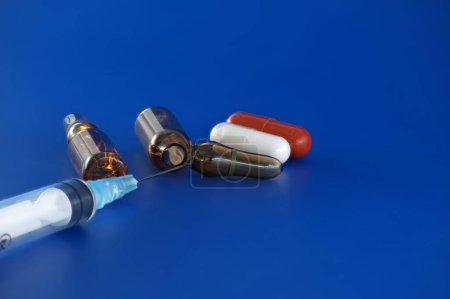 Foto de Jeringa, ampolla y pastillas contra un fondo azul, sugiere la medicación oral como una alternativa a los inyectables - Imagen libre de derechos