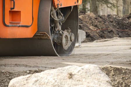Orange road roller engaged in construction work, process of asphalt laying or compaction, active roadwork