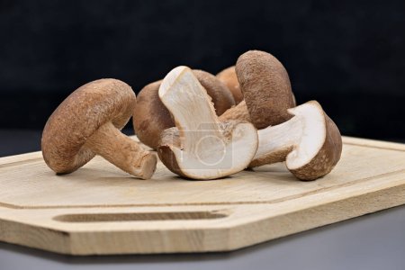 Frische Shiitake-Pilze auf Schneidebrett, ein Pilz wird geschnitten, was ihr weißes Innere, ihre gesunde Ernährung und ihre pharmakologischen Eigenschaften, Lentinula edodes, enthüllt