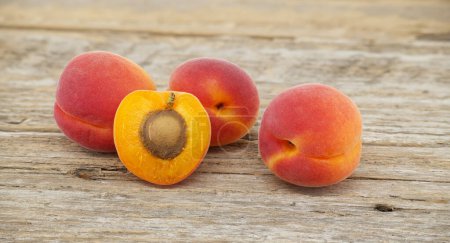 Group of fresh whole apricots and one cut in half to reveal its interior, rustic wooden table
