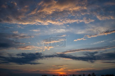 Hermosa escena de puesta de sol acentuada por un cielo lleno de nubes que reflejan diferentes tonos de rosa, naranja y azul. Estos colores crean un contraste llamativo e iluminan las nubes