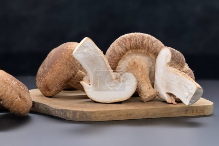 Champignons shiitake frais reposent sur une planche à découper, avec un champignon tranché ouvert pour révéler son intérieur blanc, nutritionnel et médicinal, Lentinula edodes