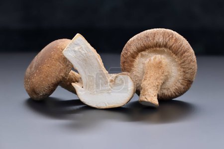 Frische Shiitake-Pilze ruhen auf einem Schneidebrett, wobei ein Pilz aufgeschnitten wird, um sein weißes Innere, seine gesunde Ernährung und seine pharmakologischen Eigenschaften, Lentinula edodes, zu enthüllen.