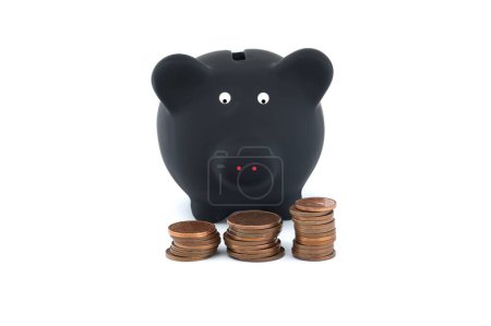 Black piggy bank is flanked by three separate stacks of coins, each stack decreasing in size from left to right, all set against a stark white background