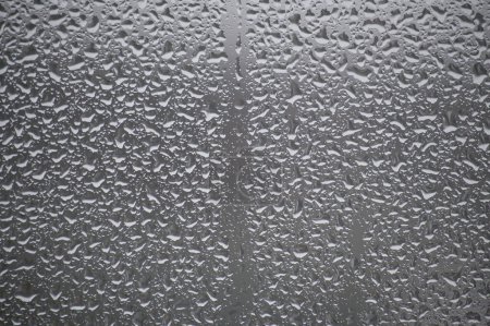 Close-up view of a glass surface covered with many water droplets of various sizes, creating a textured pattern