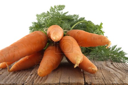 Bundle of carrots with green tops is neatly tied together using twine and positioned on an old, rustic wooden table