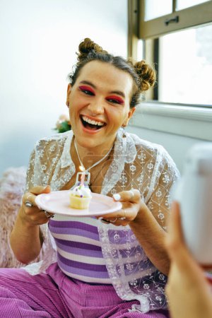 Téléchargez les photos : Joyeux jeune adulte tenant assiette avec cupcake d'anniversaire, souriant, lgbt, - en image libre de droit