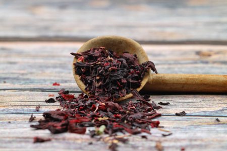 Karkade tea. Hibiscus tea leaves in wooden spoon isolated on wooden background. File contains clipping path. Top view. Selective focus.