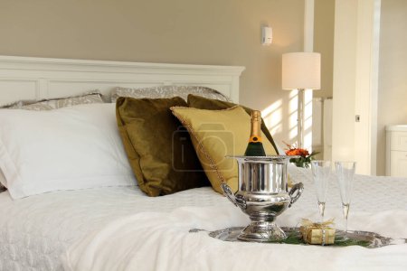 Téléchargez les photos : Bouteille de champagne sur glace sur un lit luxueux. Chambre romantique d'hôtel avec champagne et cadeau enveloppé dans l'or, placé sur la literie de couette. - en image libre de droit