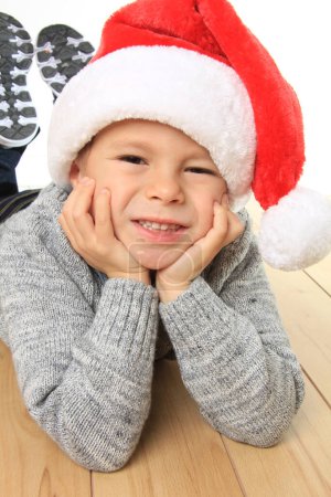 Téléchargez les photos : Joyeux garçon de cinq ans allongé sur le sol, portant un chapeau de Père Noël et attendant le Père Noël à Noël. - en image libre de droit