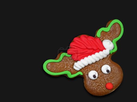 Téléchargez les photos : Biscuit de renne de Noël, rudolph avec chapeau santa pain d'épice isolé sur fond noir avec espace de copie. - en image libre de droit