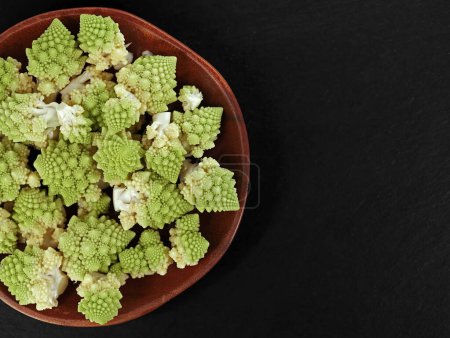 Photo for Top view of fresh romanesco florets in wooden bowl on black slate plate with copy space, preparation of healthy cabbage vegetable. - Royalty Free Image