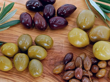 Close up of different types of olives on a wooden serving plate, mixed olives of different sizes as a healthy appetizer.