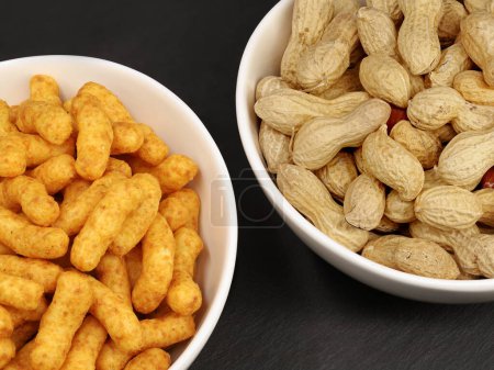 Photo for Portion of peanut flips and naturally roasted inshell peanuts in white bowls on black background, snack comparison of peanuts. - Royalty Free Image